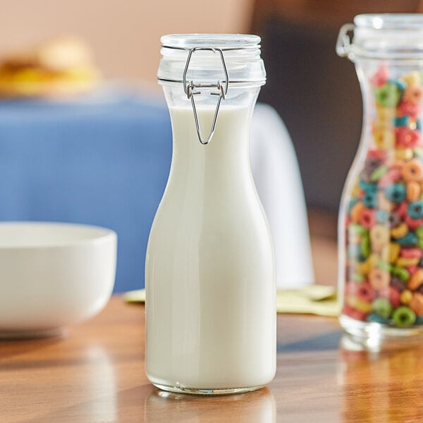 An Acopa glass carafe filled with milk on a table with a bowl of cereal.