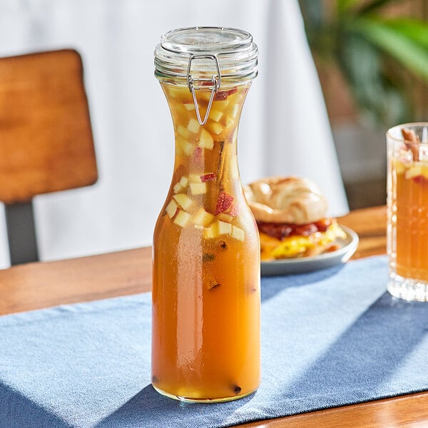An Acopa glass carafe filled with orange liquid and fruit on a table.
