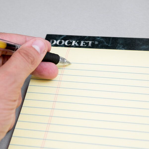A hand writing with a pen on a yellow lined Docket writing pad.