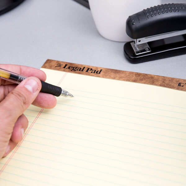 A hand holding a pen writing on a TOPS wide ruled legal pad.