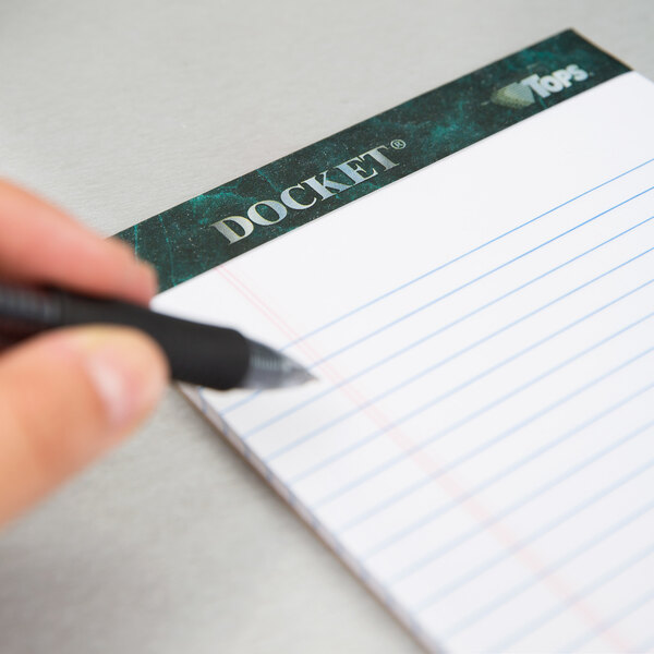 A hand holding a pen writes on a TOPS Docket notepad.