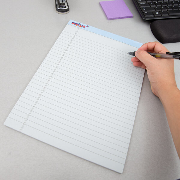A hand holding a pen writing on a blue legal pad.