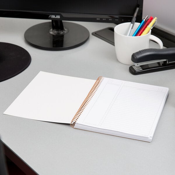 A black spiral bound planner on a desk with a pen in it.