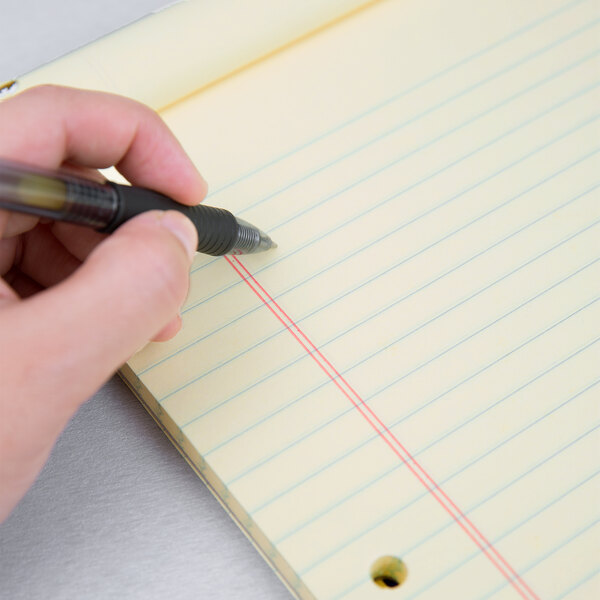 A person writing with a pen on a medium ruled Ampad writing pad.