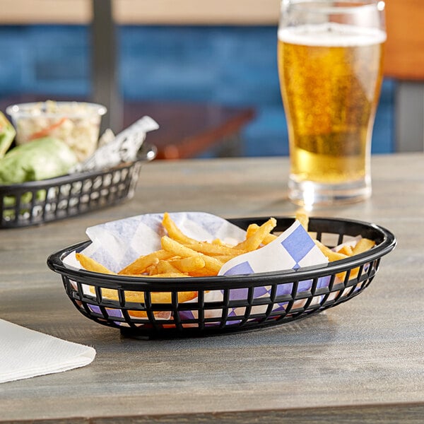 A Tablecraft black plastic oval basket filled with french fries on a table in a fast food restaurant.