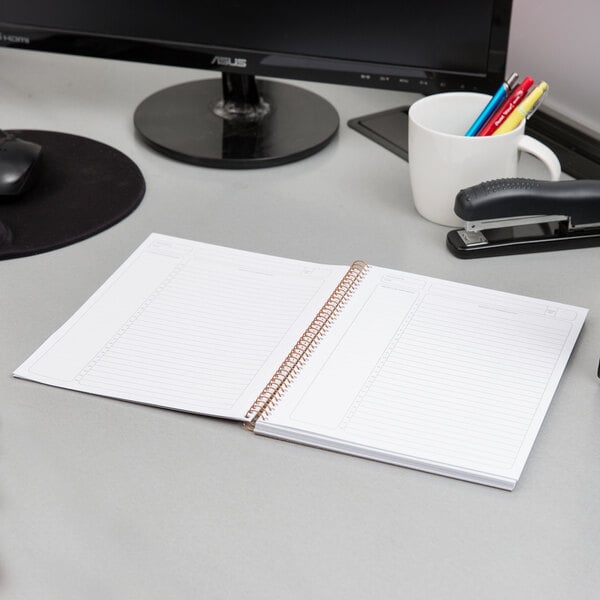 A spiral bound Ampad project planner with a green cover on a table with a pen nearby.