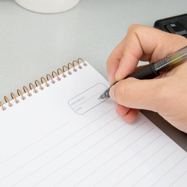 A hand writing on an Ampad wirebound planner pad with green cover.