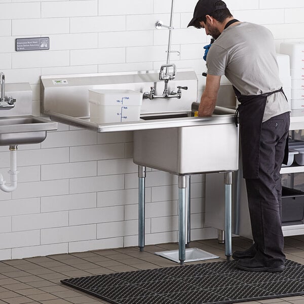 A man in an apron standing at a Regency stainless steel sink in a professional kitchen.