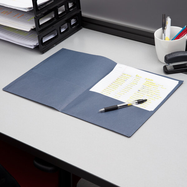 An Oxford dark blue paper pocket folder on a desk with paper and pens inside.