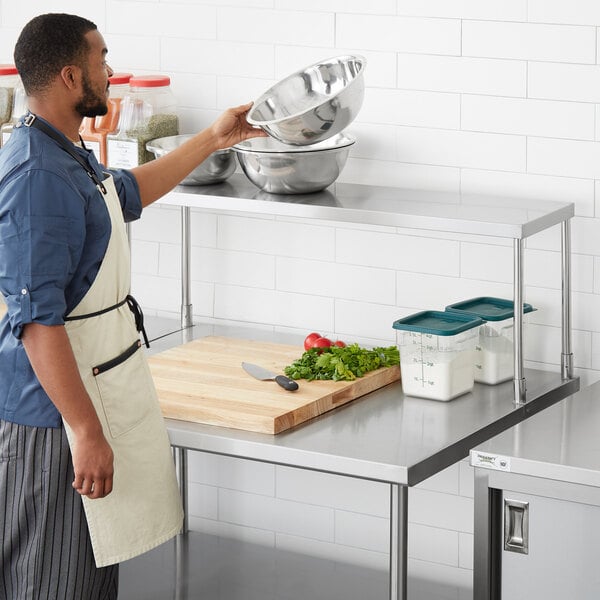 A man in an apron using a Regency stainless steel single deck overshelf on a stainless steel table.