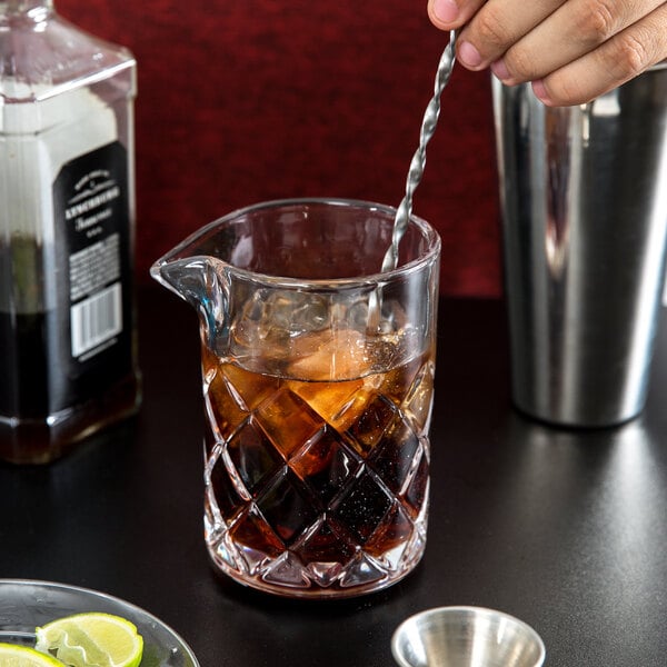 A person using an Arcoroc stirring glass to pour a drink from a pitcher.