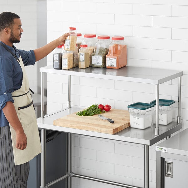 A man in an apron standing next to a Regency stainless steel table mounted overshelf.
