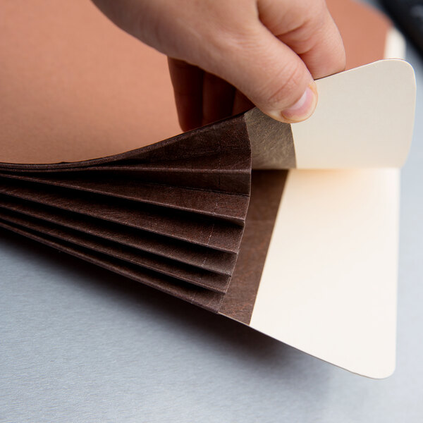 A hand cutting a brown Pendaflex heavy-duty file pocket with a knife.