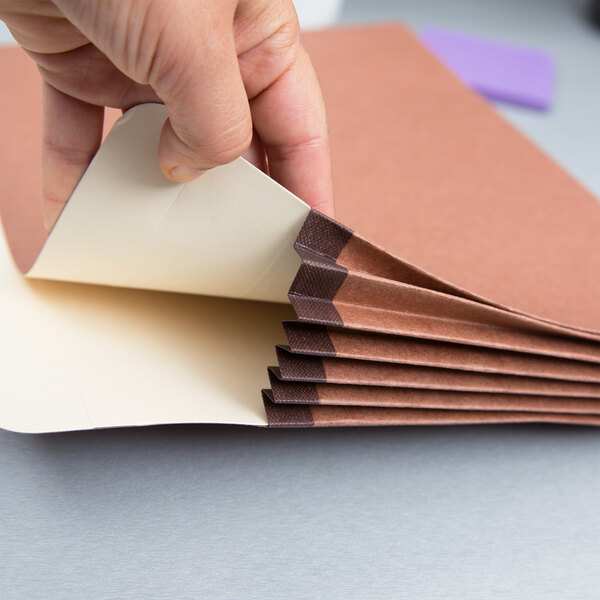 A person holding a piece of paper with a brown Pendaflex file pocket.