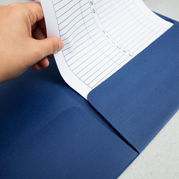 A hand placing a piece of paper in a navy blue Oxford pocket folder.