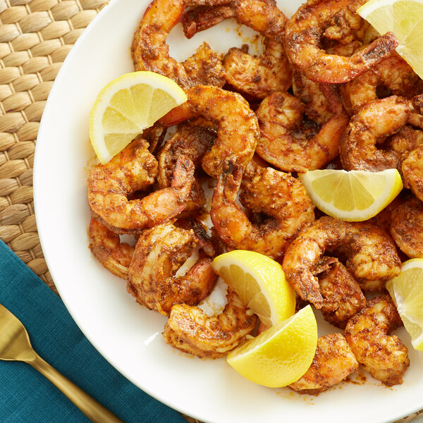 A plate of Old Bay seasoned shrimp with lemon wedges.