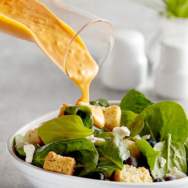 A bowl of salad with orange liquid being poured over it.