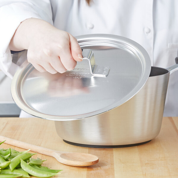 A person holding a Vollrath aluminum lid over a pot.