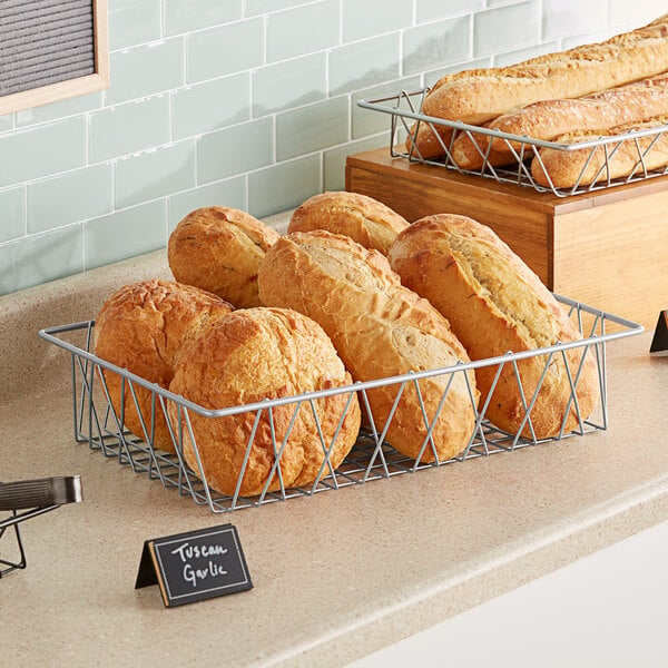 A silver wire pastry basket filled with loaves of bread on a counter in a bakery display.