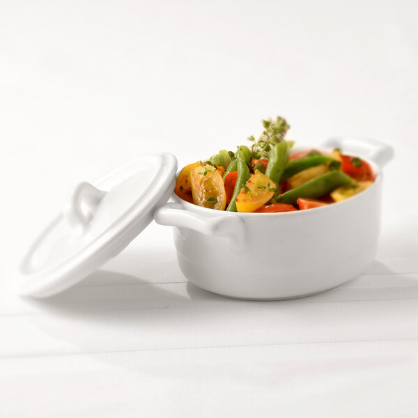 A white Bon Chef oval cocotte filled with vegetables with a white lid.