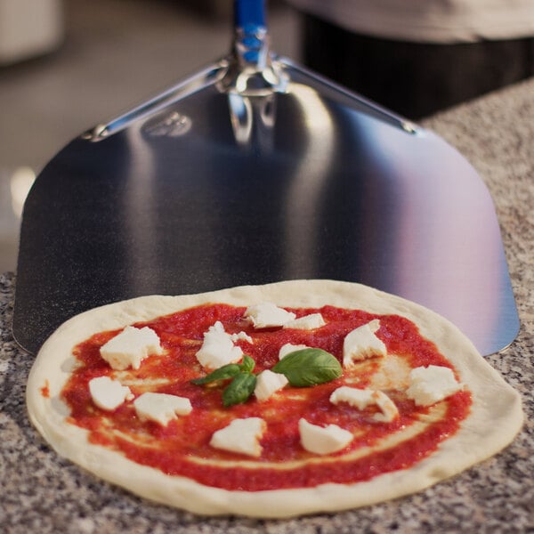 A pizza with cheese and basil on it being removed from a counter with a GI Metal square pizza peel.