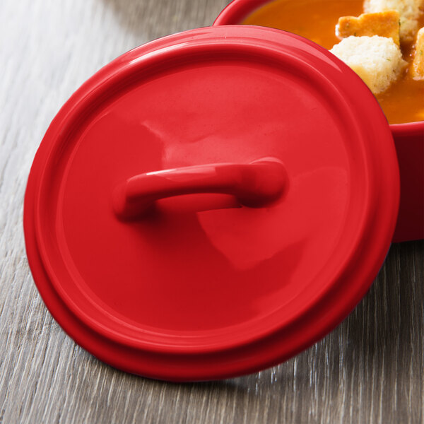 A red Bon Chef porcelain lid on a bowl of soup.