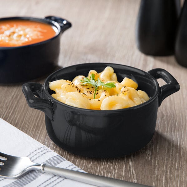 A matte black porcelain cocotte filled with macaroni and cheese next to a fork.