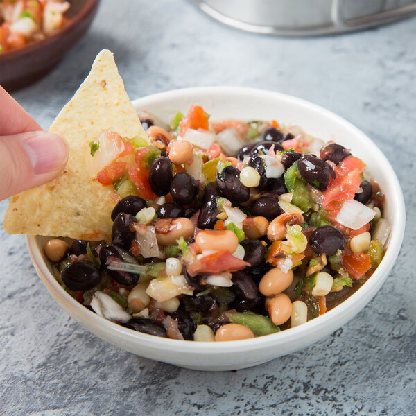 A person holding a chip dipping it into a bowl of black bean and corn salsa.