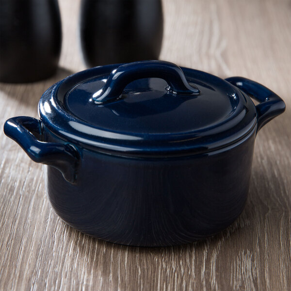 A cobalt blue Bon Chef porcelain cocotte lid with two black handles.