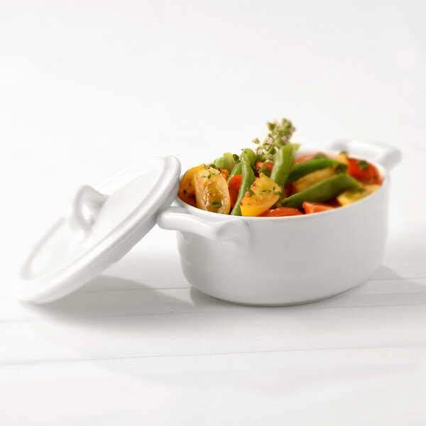 The white lid of a Bon Chef white porcelain cocotte over a pot of vegetables.