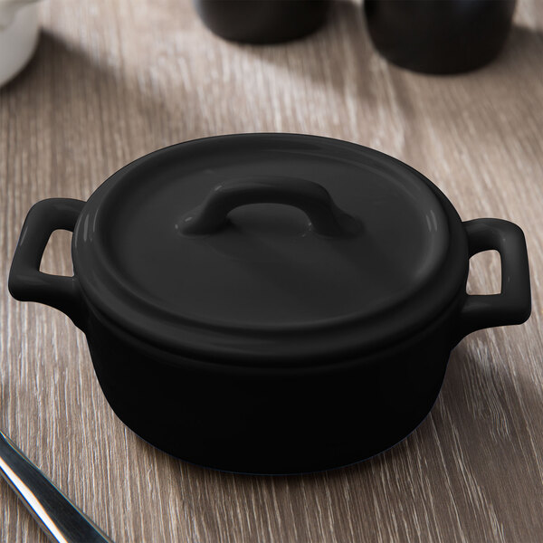 A matte black Bon Chef oval cocotte with a lid on a wood surface.