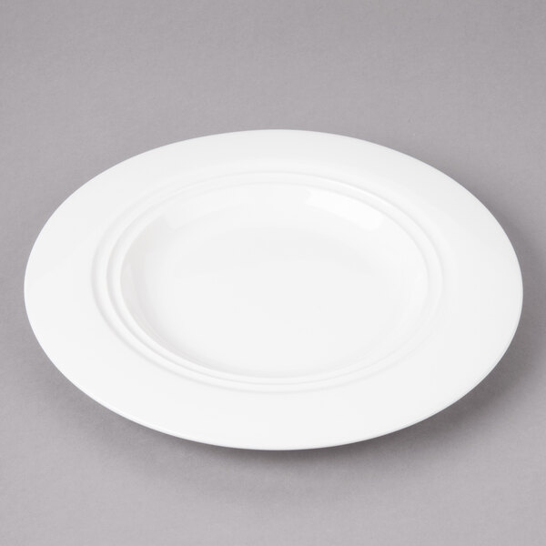 A white Bon Chef round porcelain plate with a rim on a gray surface.