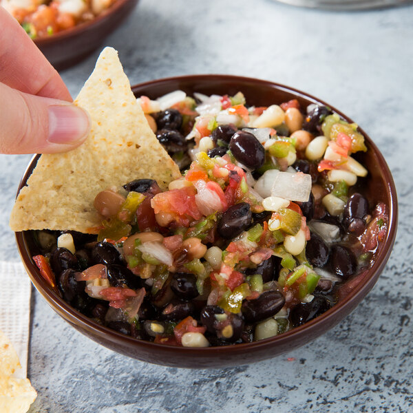 A person holding a chip dips it into a bowl of salsa.