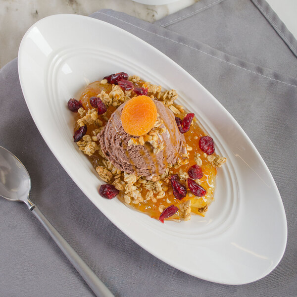 A white porcelain bowl filled with ice cream, granola, and fruit with a spoon next to it.