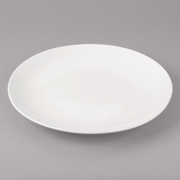 A white Bon Chef porcelain dinner plate with a white circle on the rim on a gray surface.