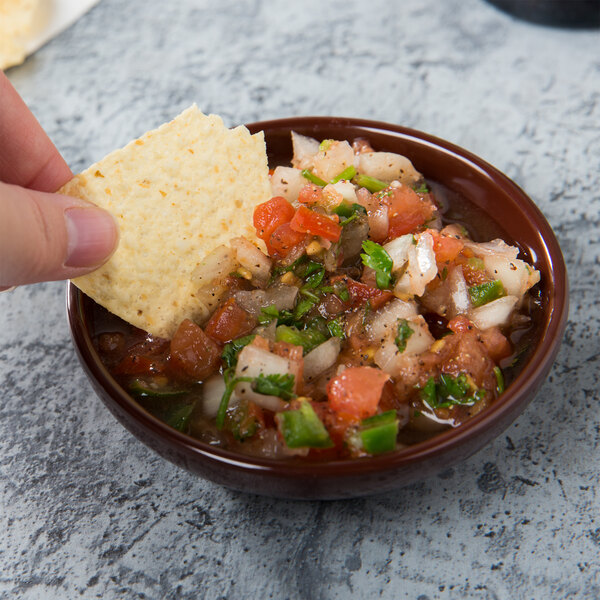 A hand holding a chip over a bowl of chocolate salsa.