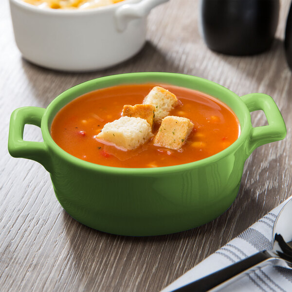 A lime porcelain oval cocotte filled with soup and croutons.