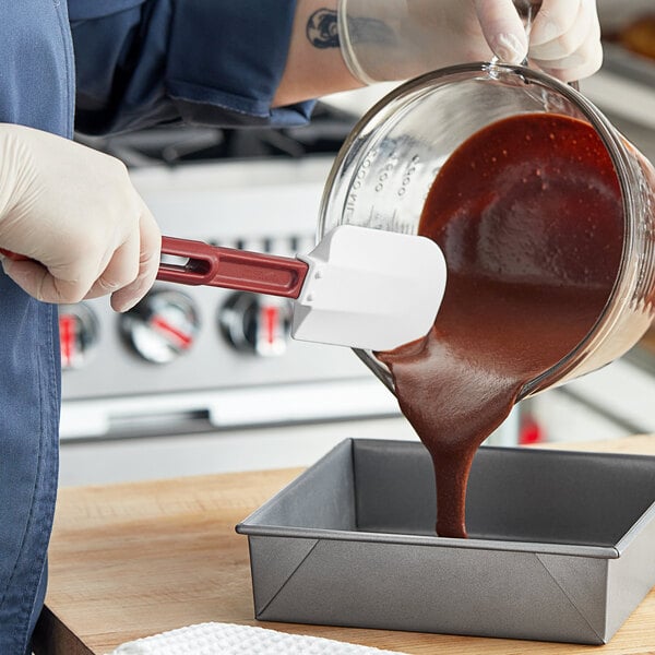 A hand using a Vollrath high heat silicone spatula to pour brown liquid into a pan.