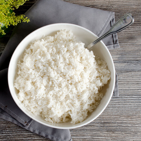 A white Bon Chef porcelain bowl filled with rice with a spoon in it.