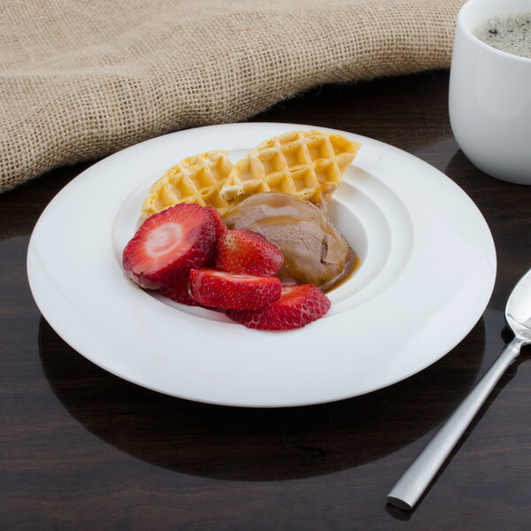 A plate of waffles with strawberries and a Bon Chef white porcelain bowl on a table.