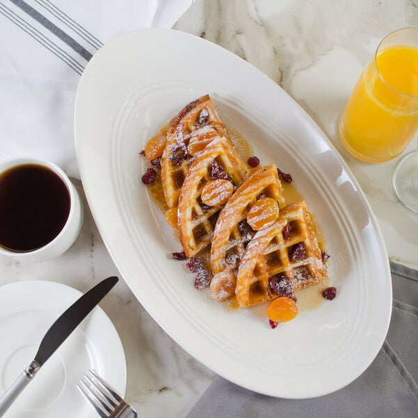 A white porcelain plate with a waffle topped with fruit and powdered sugar next to a cup of coffee.