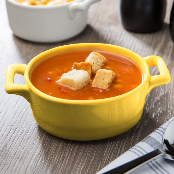 A yellow Bon Chef porcelain oval cocotte filled with soup and croutons.