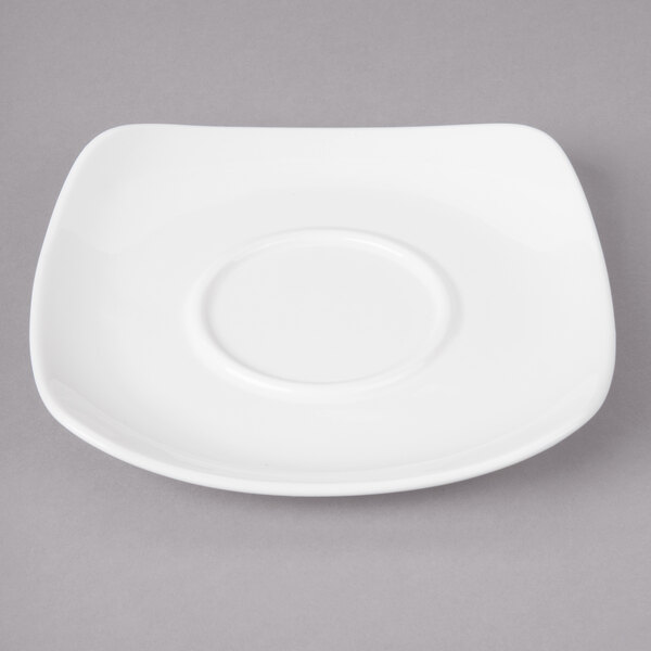 A white square plate with a round white porcelain saucer on it.
