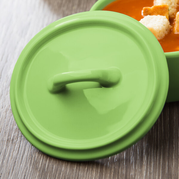 A Bon Chef lime porcelain oval cocotte lid with a handle on a bowl of soup.
