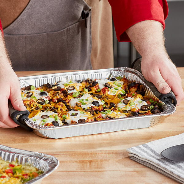 A person using a Western Plastics shallow foil steam table pan to serve a meal.