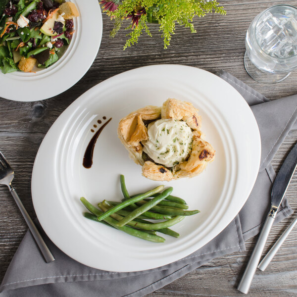 A Bon Chef white porcelain oval dinner plate with a plate of food on a table.