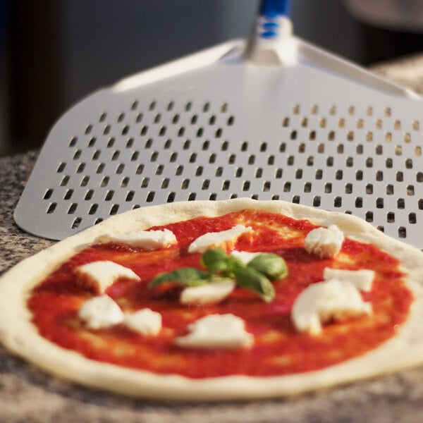 A pizza on a GI Metal square perforated pizza peel with cheese and basil on it.