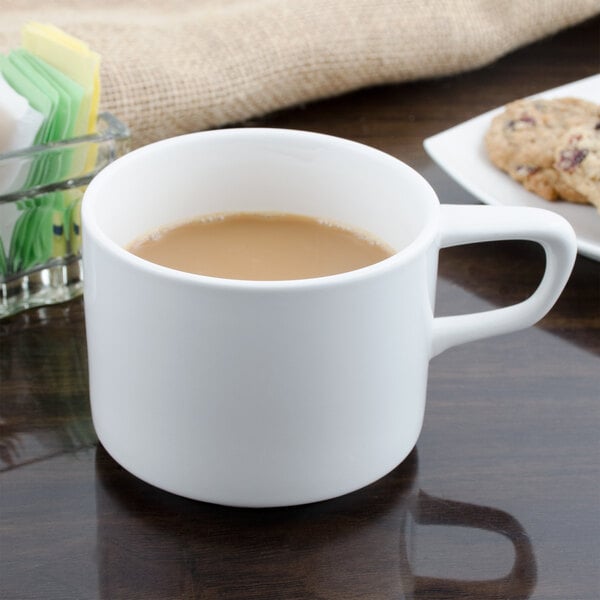 A white Bon Chef slanted oval porcelain cup filled with coffee sits on a saucer next to cookies.