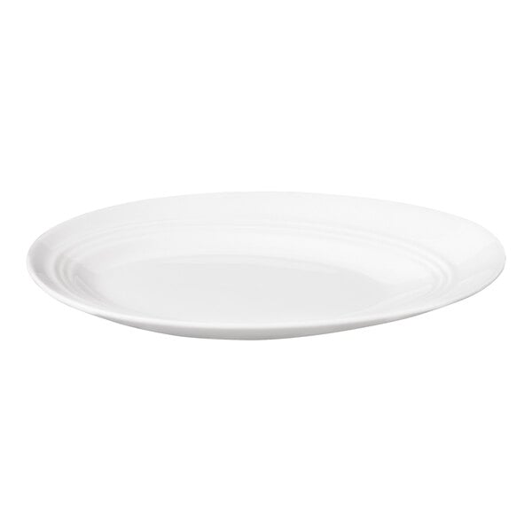 A white, oval-shaped porcelain plate with a slightly slanted rim and subtle concentric detailing.