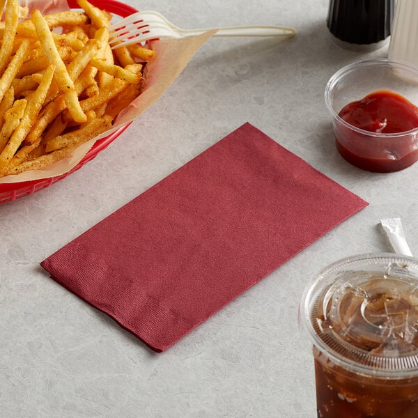 A basket of french fries with a burgundy Choice paper napkin next to a drink.